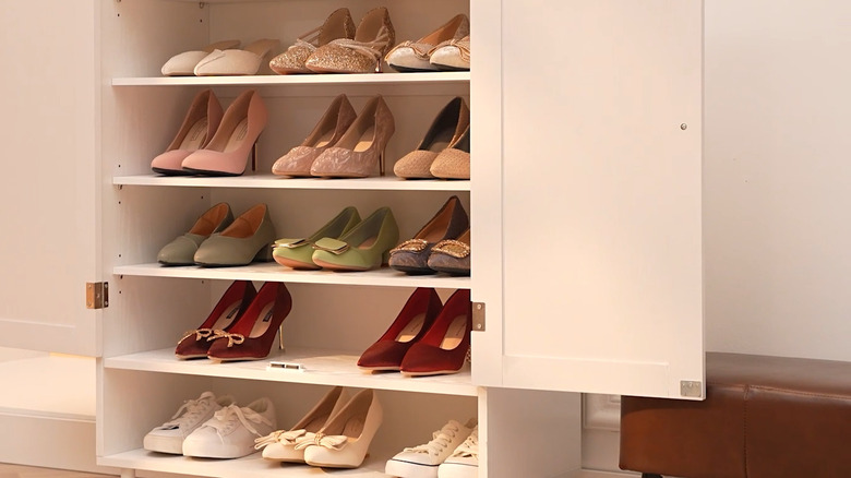 A white shoe storage cabinet with high heels on the shelves in a hallway.