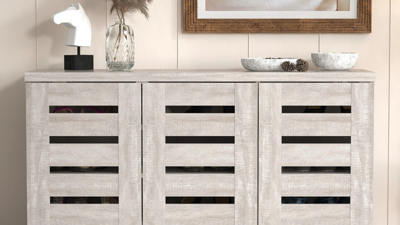 A 20-pair shoe wood-finish cabinet with slats in the door for ventilation and decor on top in a home.
