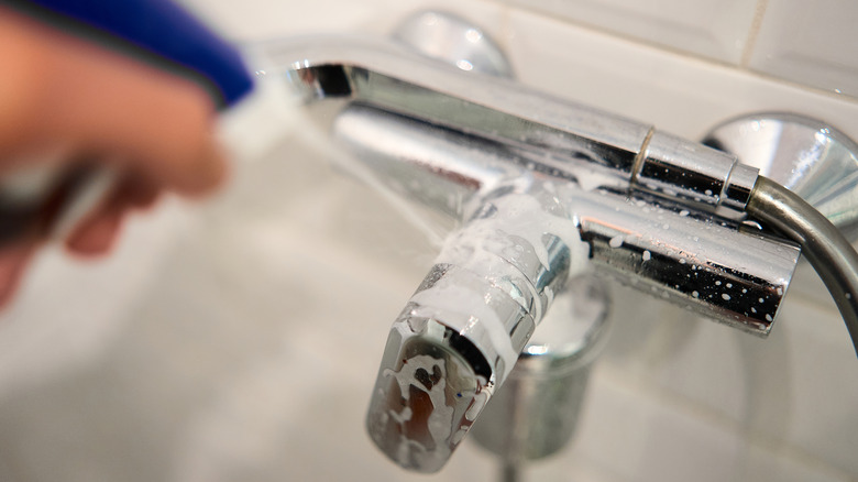 Spraying chrome bathroom faucet with cleaner