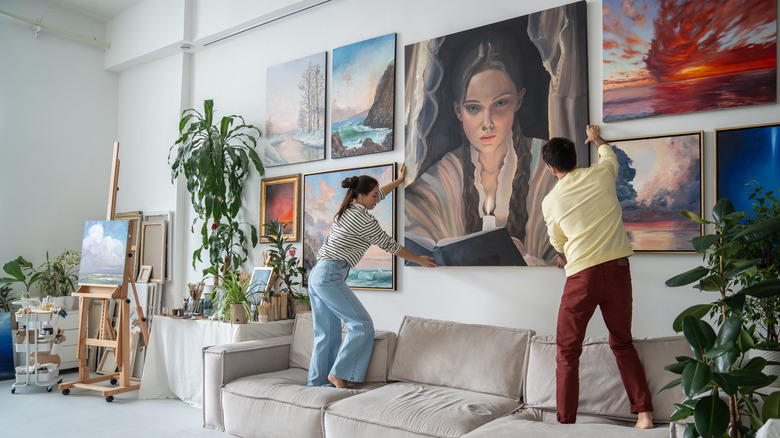 Two people hanging a gallery wall with one large painting at center