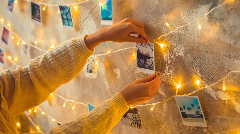 Hands hanging memories and mementos on wall with Christmas lights