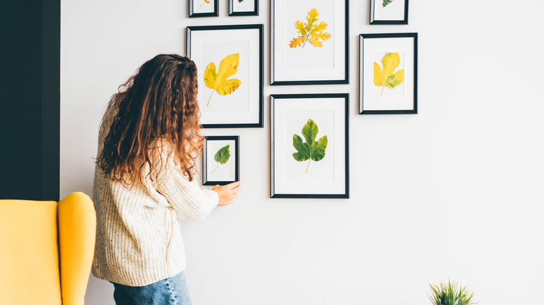 A woman hanging framed leaves on wall