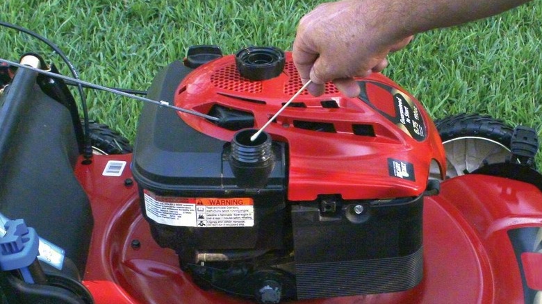 A person pulling a swab about of a gas tank of a lawn mower