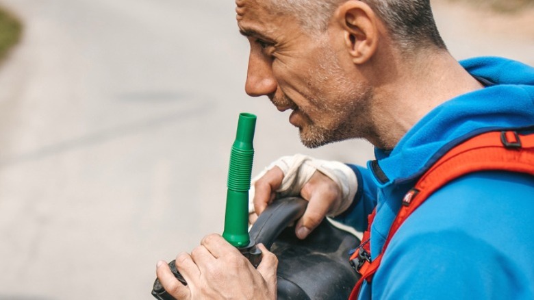 A man smelling gas can nozzle to check for expired gas odor