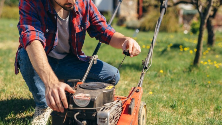 A man checking his push mower oil and other components