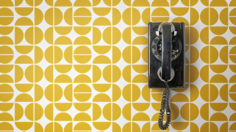 Vintage wall mounted rotary telephone with coil cord on a retro designed wall