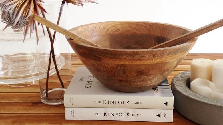 Empty wooden salad bold over sat on top of cooking books over wooden table.