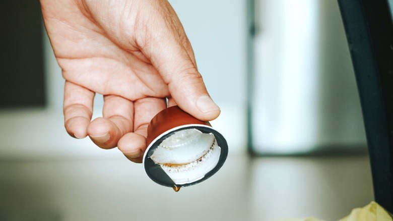 Person holding empty coffee pod over garbage can