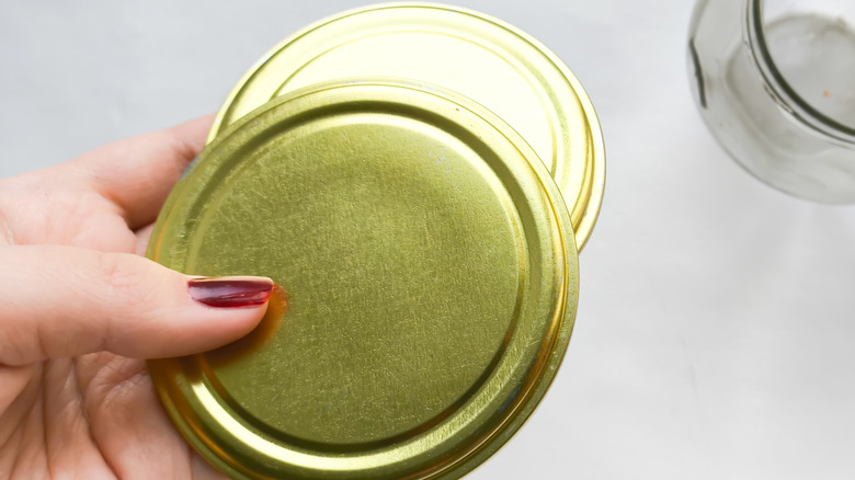 Hand holding two gold jelly jar lids
