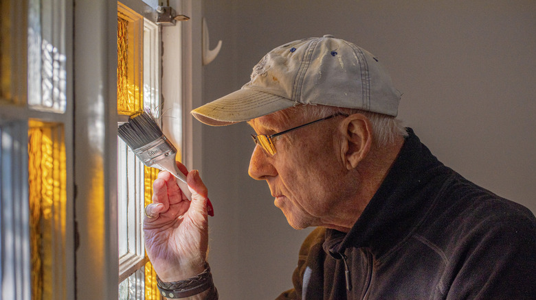 Older man painting on glass windows wearing a hat
