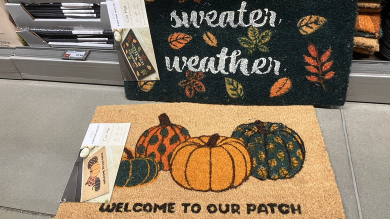 Two coir welcome mats, one reading "sweater weather" and the other reading "welcome to our patch" with pumpkins.