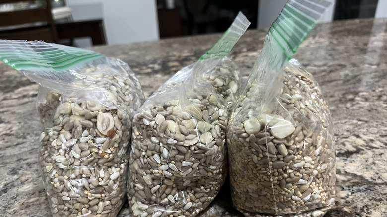 Three plastic zippered bags of bird seed mix on a granite countertop