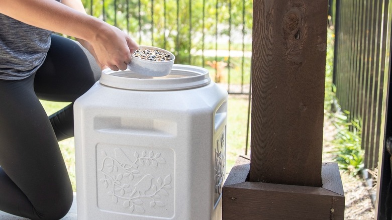 Woman's hand dipping into a heavy-duty plastic storage container of bird seed on a porch