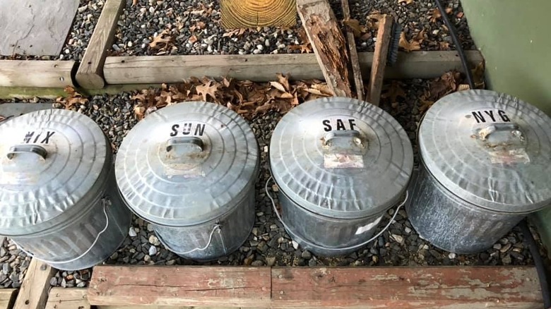 Galvanized metal cans labeled with bird seed name outside between blocks of wood