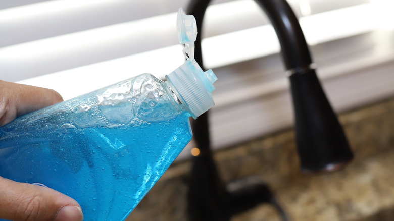 Close up of person pouring blue dish soap onto sponge