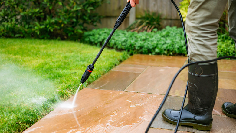 Close up of person using pressure washer to spray down cement tile