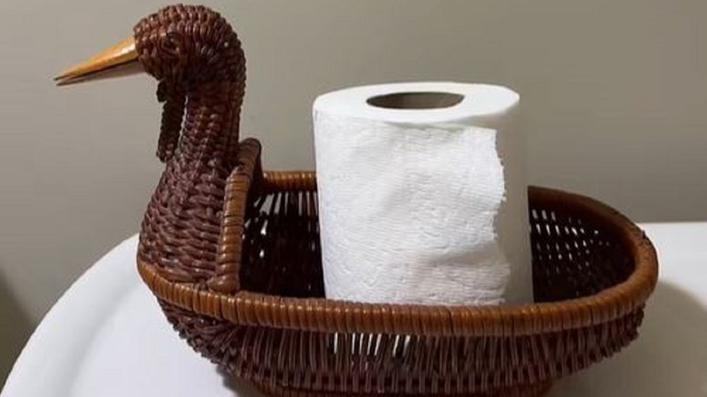 Duck basket on back of toilet holding toilet paper