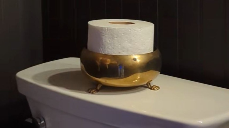 Toilet paper roll sitting in thrifted brass bowl on back of toilet