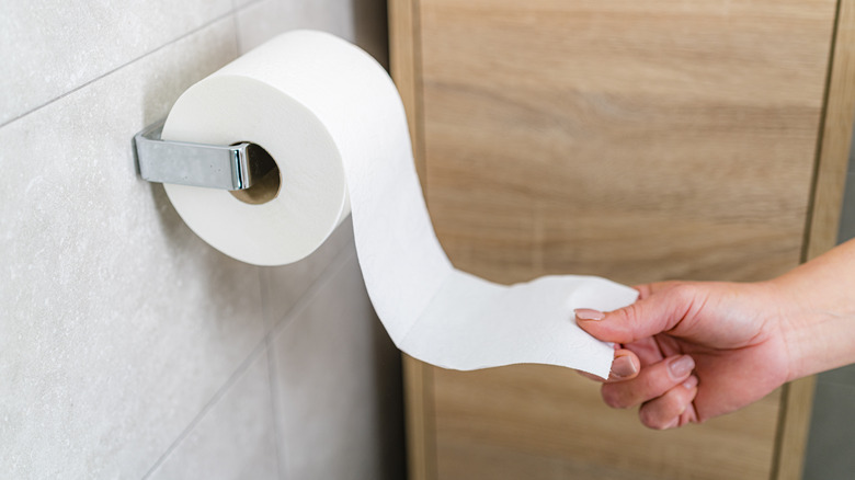 Person pulling on toilet paper in bathroom