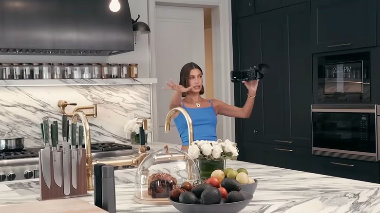 Hailey Bieber vlogging in her black and white kitchen with marble slab backsplash