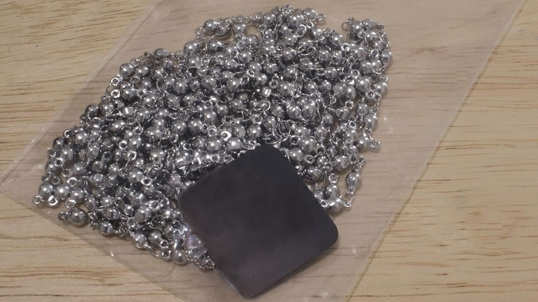 A black anti-tarnish strip or tab inside a sealable plastic bag with a silver chain necklace.