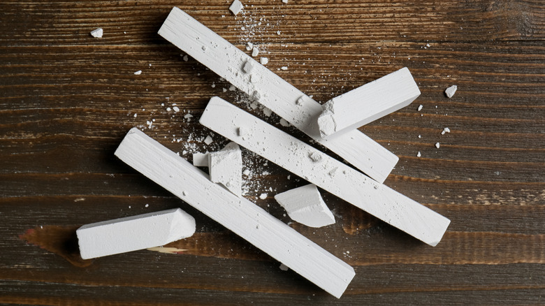 Pieces of whole and broken chalk on a wooden tabletop.