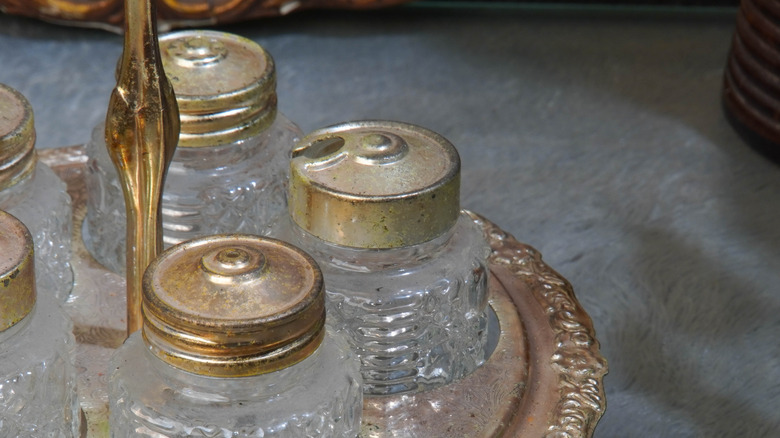 A tarnished silver and glass condiments set on a tarnished sliver tray with a handle.
