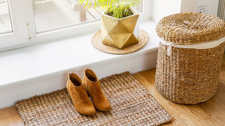 Woven basket with lid by a doorway with a pair of shoes on a jute entryway rug