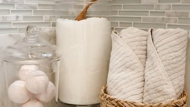 Vase used to store bath salt next to a basket of rolled towels and jar of bath bombs