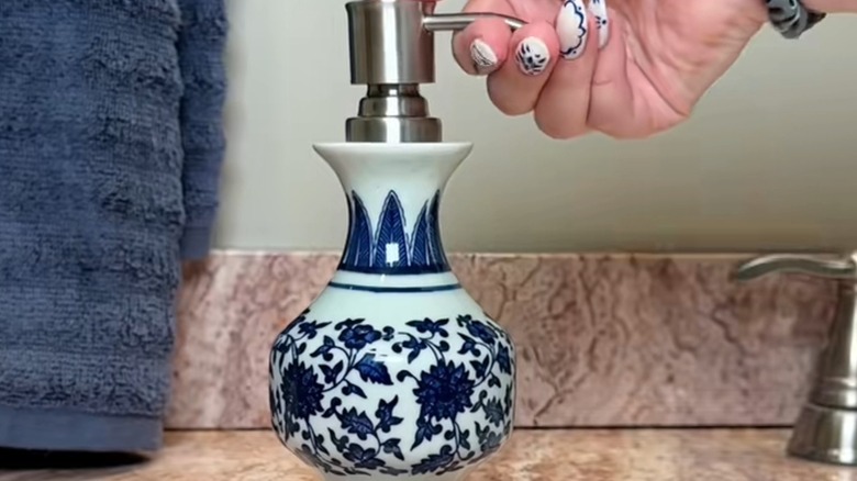Woman's hand using a blue and white ceramic vase turned soap pump