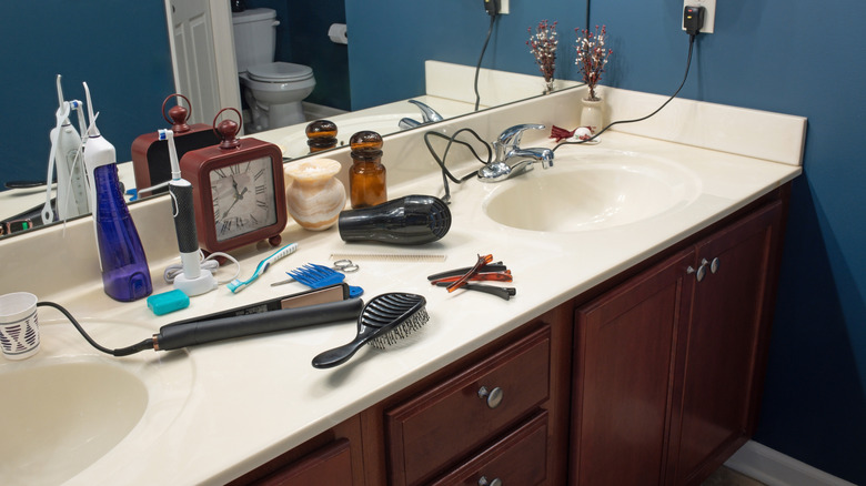 Bathroom counter covered with a toothbrush, hair dryer, straightened, hair clips, and other needs