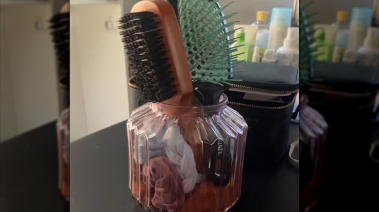 View of hairbrushes and scrunchies in a pink glass vase