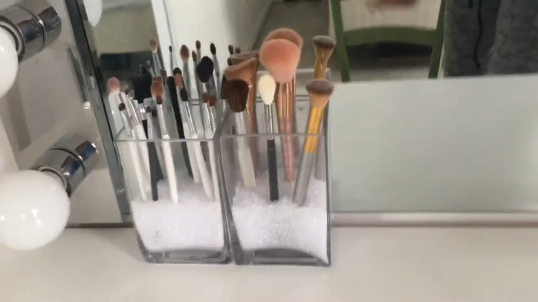 Glass square vases filled with craft sand and used to elevate makeup brushes
