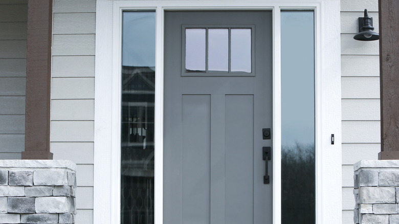 Light gray front door with window on a gray clapboard house