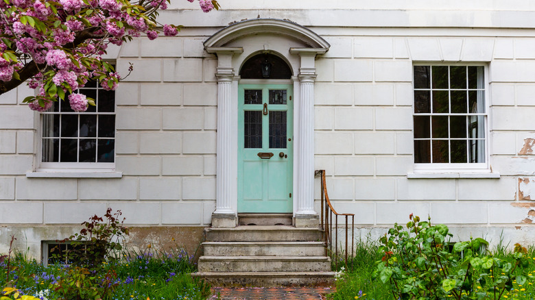 Pastel green front door with columns and pediment on a white stone house