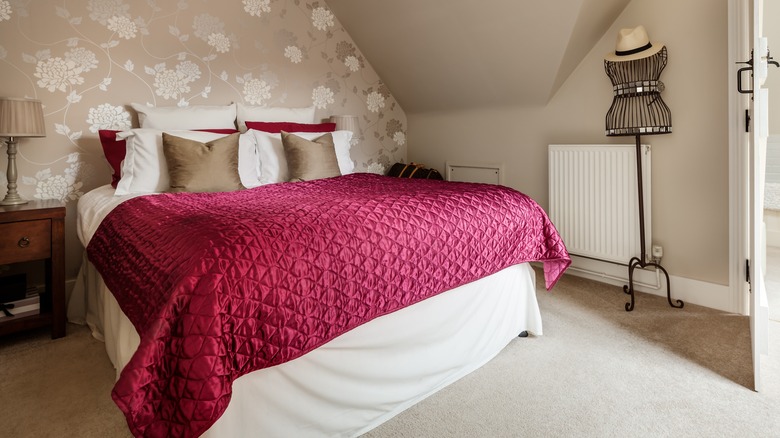 A rich ruby red jewelled comforter on a bed with beige and white cushions.