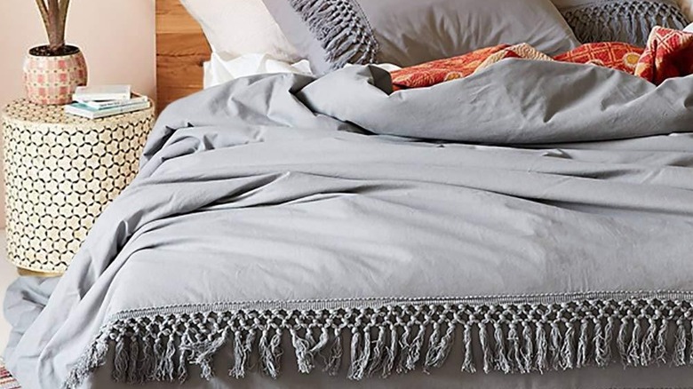 A grey texture comforter on a bed with a quirky patterned bedside table.