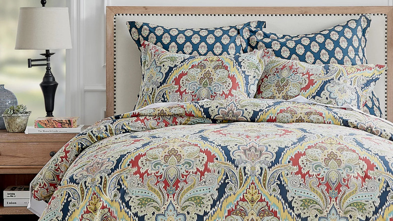 A vibrantly patterned comforter and matching pillows with red, blue and yellow patterns on a off-white background.