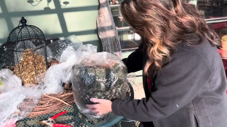 A woman covers a potted plant in a plastic garbage bag.