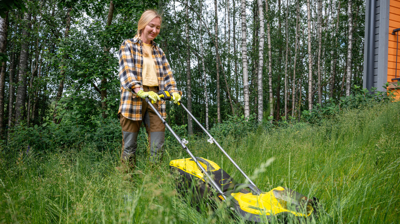 A woman pushing a yellow mower cuts down tall grass