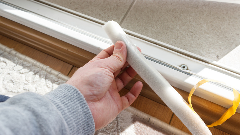 A person is seen fixing the threshold of a doorway with weatherstripping