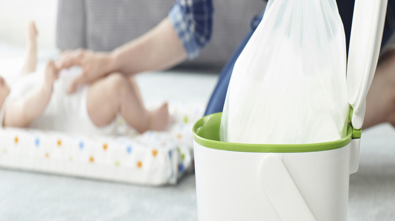 A woman changes a baby and throws the dirty diaper away