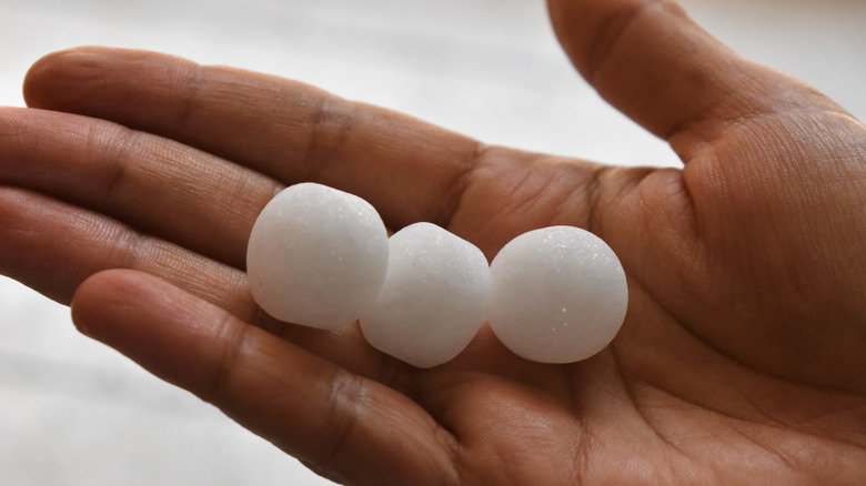 A person's hand is holding three mothballs