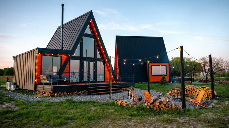 Two miniature A-frame cabins on a plot of land with a fire pit.