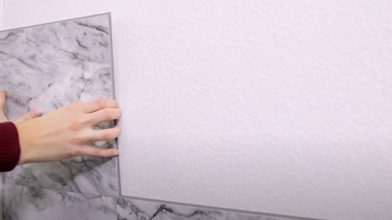 Hands installing marble vinyl tiles on wall