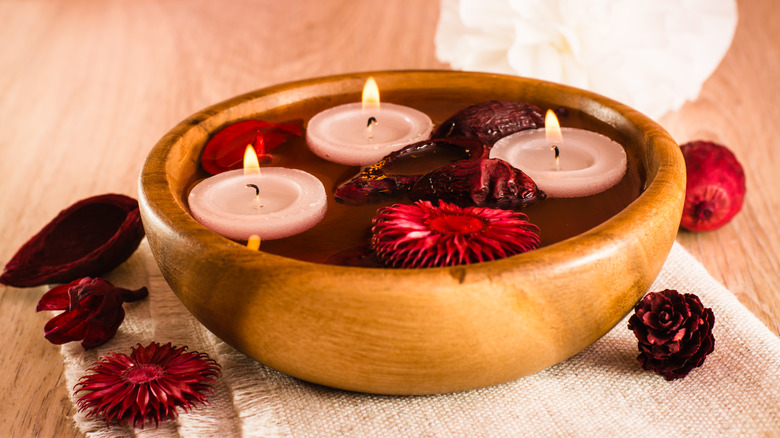 Close up of candles floating in wooden bowl with flower petals