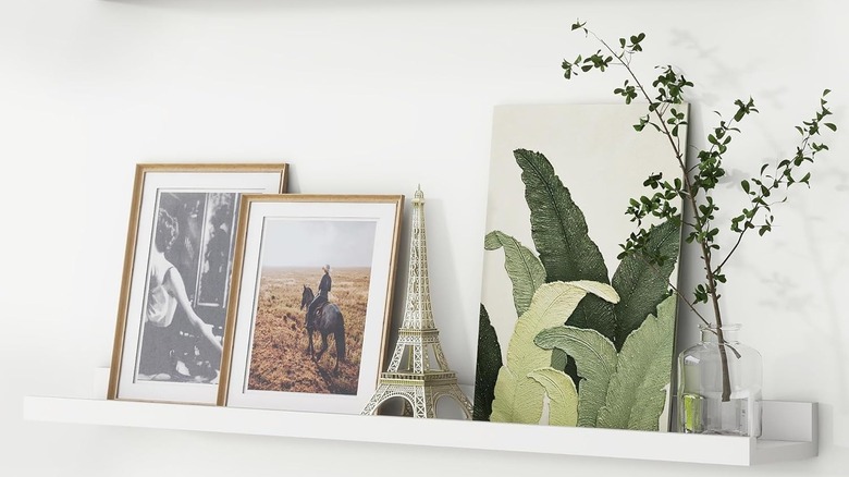 A white photo ledge with photos and a plant sitting on it.