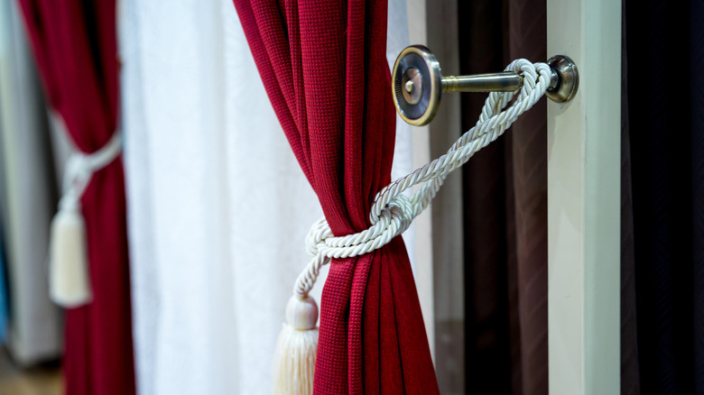 A close up of a curtain tie back holding a red curtain with white decorative rope
