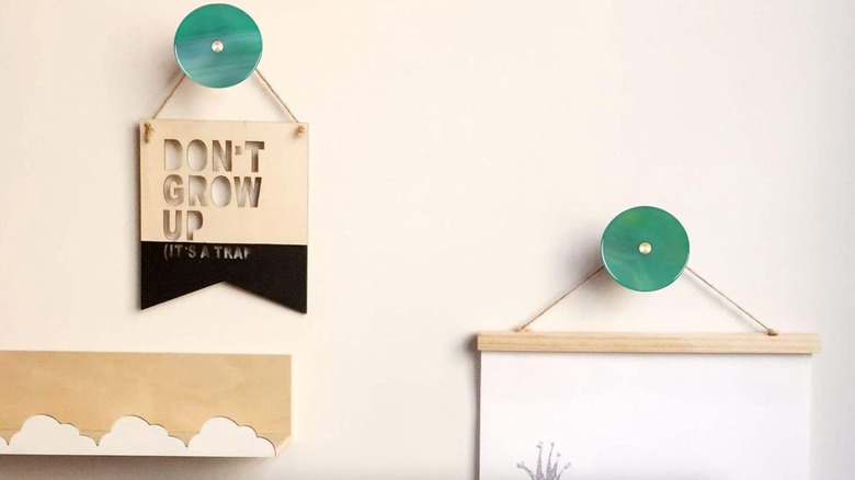 Two decor pieces hang from two teal, round curtain tie backs on the wall