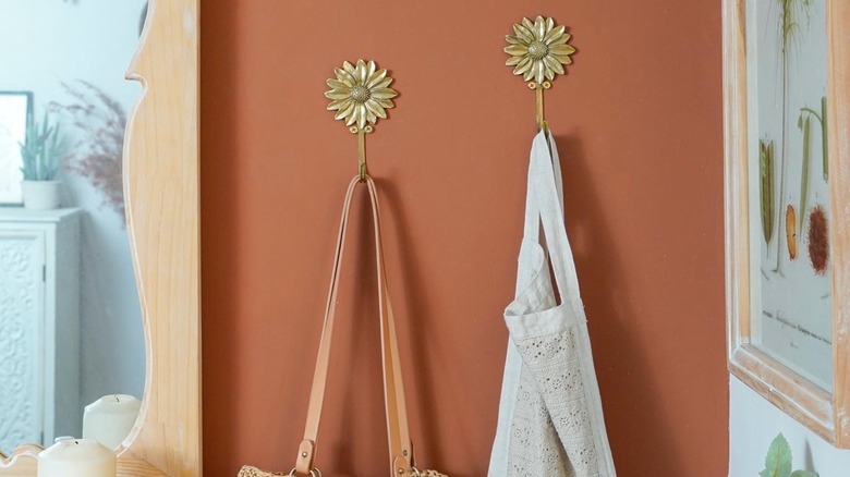 Two flower tie backs hold a bag and an apron on an orange wall in a tight space